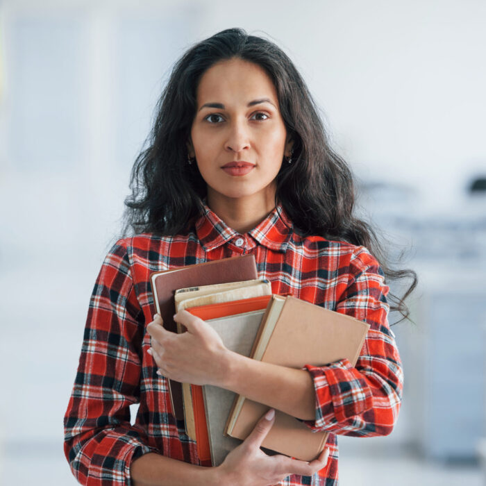 Vertical photo of attractive young woman standing in the office and holding books and documents.